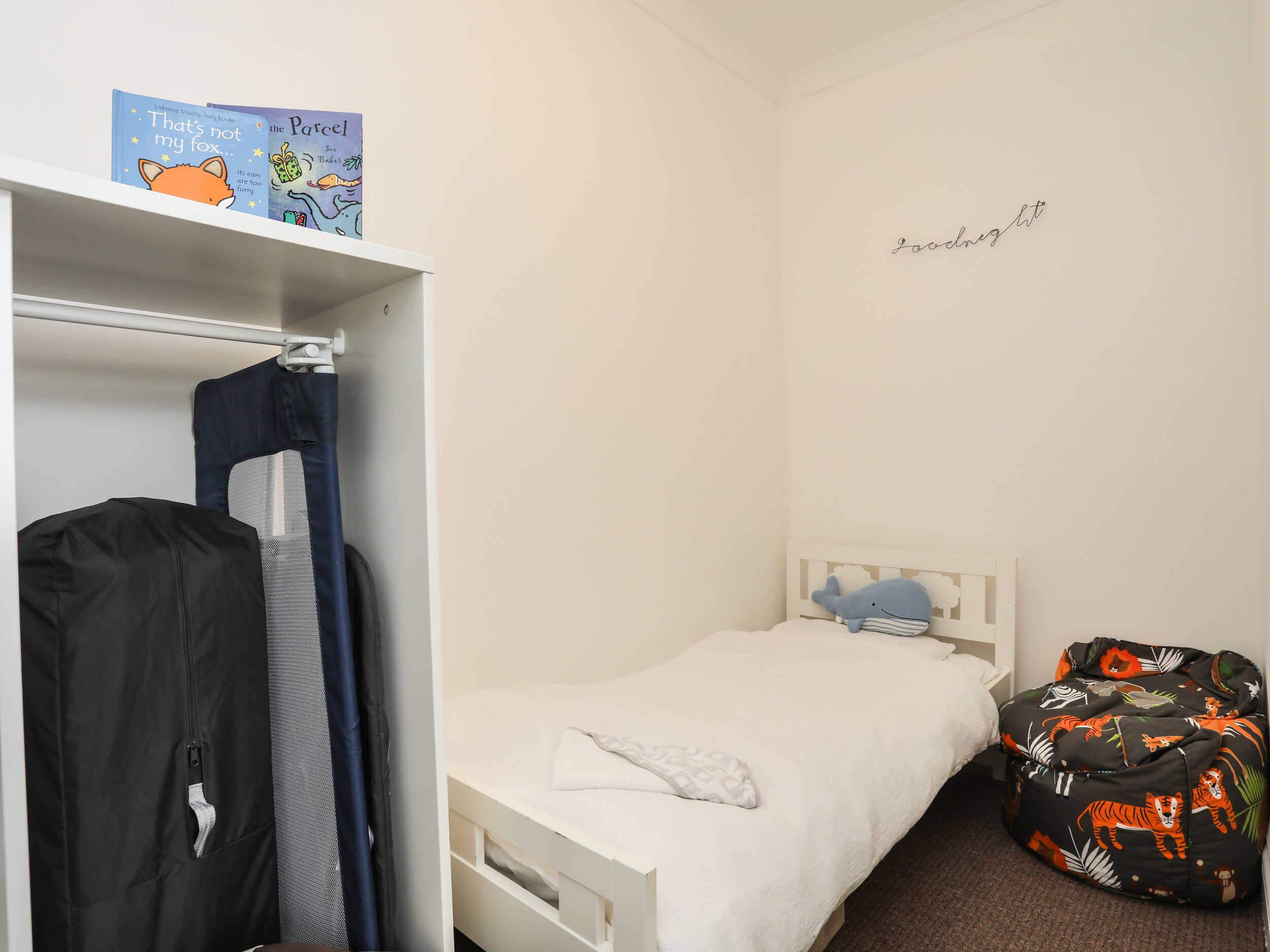 A bedroom with a single bed, a wardrobe, and a small seating area with a plush toy.