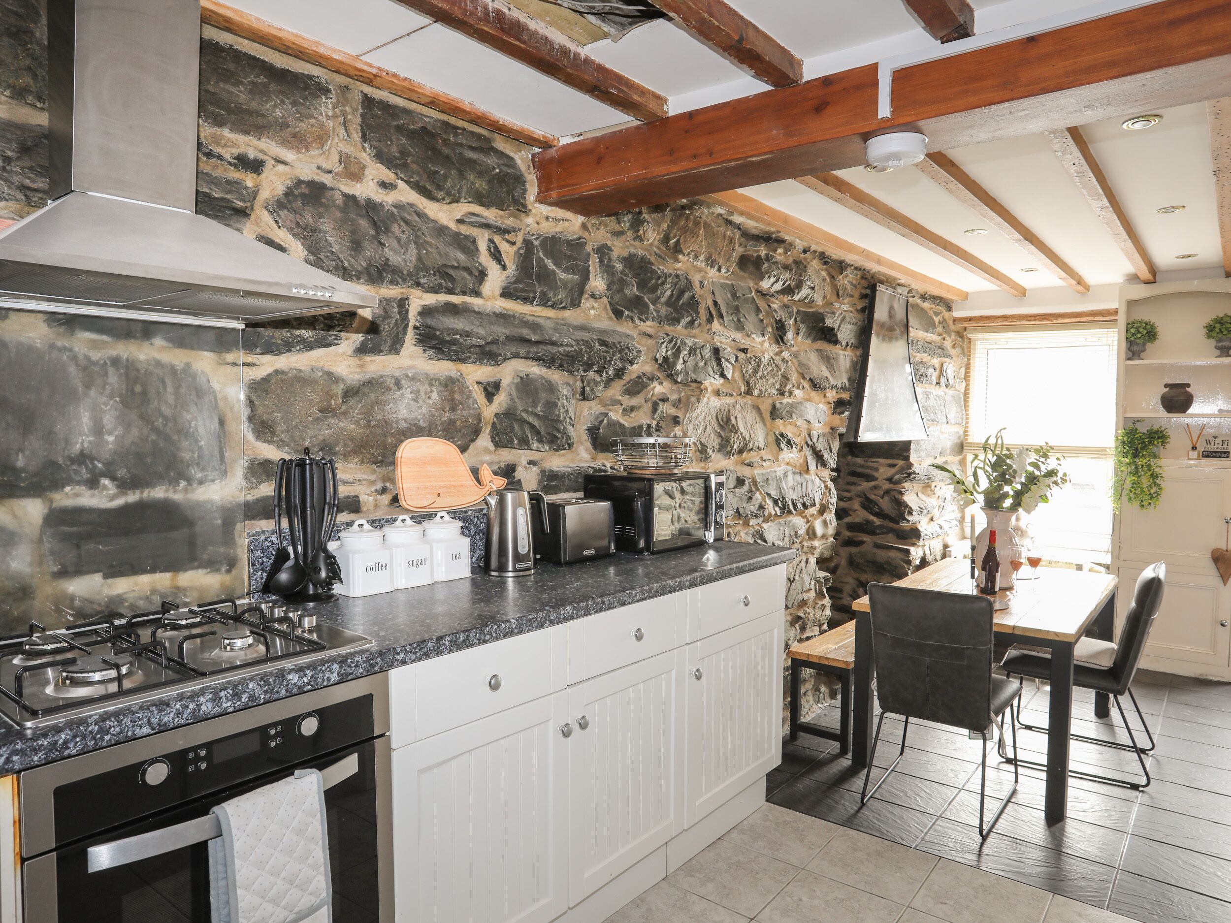 Una cucina con parete in pietra, piano cottura a gas, forno a microonde e tagliere in legno.