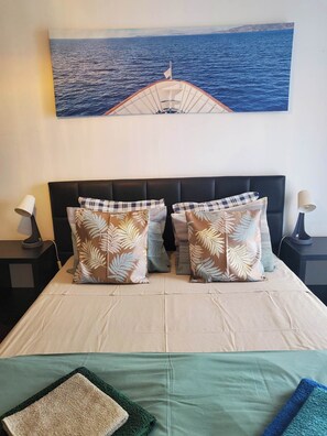 A bed with a view of the sea through a window, a black headboard, and two nightstands with lamps.