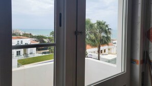 A view from a window with a view of the sea, buildings, and a palm tree. - Sunset View Apartment - 22 (Albufeira)