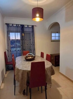 A dining area with a round table, red chairs, a basket, and a hanging light fixture.