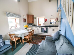 A cozy kitchen with wooden cabinets, a dining table with chairs, a gray sofa, and a blue staircase.
