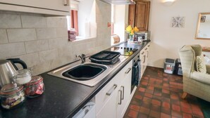 A kitchen with a black countertop, stainless steel sink, and white cabinets. There are jars on the counter and a window with curtains. - Glaisdale (Whitby)