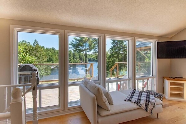 Una habitación con sofá blanco, ventanas amplias y vistas a una terraza y árboles.