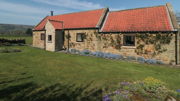 A stone house with a red-tiled roof, a stone chimney, and a small garden with flowers. - Silver Birches (Whitby)