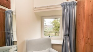 A corner room with a window, a chair with a floral pillow, and a wooden door. - Silver Birches (Whitby)