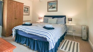 A bedroom with a large bed, wooden wardrobe, two bedside tables with lamps, a framed picture on the wall, and a standing heater. - Silver Birches (Whitby)