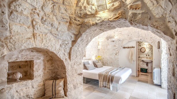 A stone-walled bedroom with a bed, a bench, and a small shelf. - Trulli, cicale e olive - Le Case di Valentina (Ceglie Messapica)