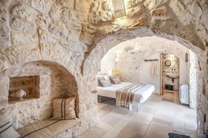 A stone-walled bedroom with a bed, a bench, and a small shelf. - Trulli, cicale e olive - Le Case di Valentina (Ceglie Messapica)