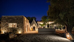 A stone building with a small arched entrance, a large vase, and outdoor seating. - Trulli, cicale e olive - Le Case di Valentina (Ceglie Messapica)