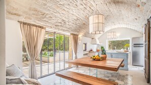 A spacious kitchen with a large island, a dining area with a wooden table and benches, and a view of the outdoors through large windows. - Trulli, cicale e olive - Le Case di Valentina (Ceglie Messapica)