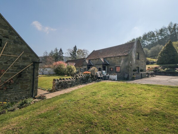 A stone building with a tiled roof, surrounded by a grassy area and a stone wall.