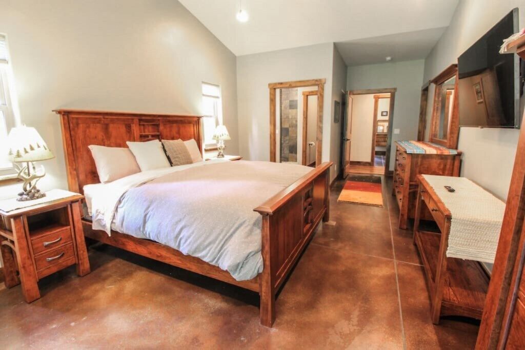 Une chambre à coucher avec un lit en bois, des tables de chevet, une commode, un miroir et un téléviseur.