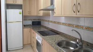 Una cocina con gabinetes de madera, un lavamanos de acero inoxidable, un microondas y un refrigerador.
