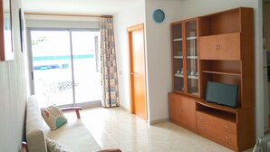 Una sala de estar con un sofá, un televisor sobre un mueble de madera y un ventanal corredero que da a un balcón.