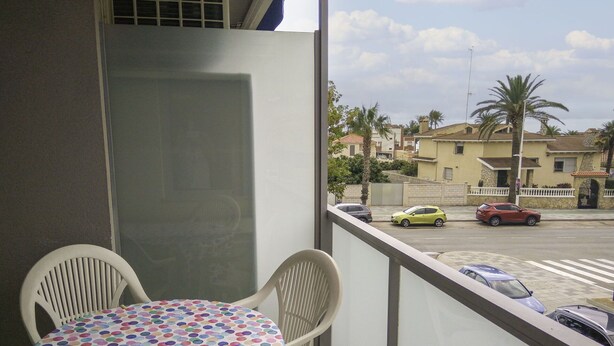 Un balcón con mesa y sillas, con vista a una calle con coches estacionados y edificios.