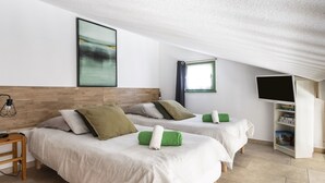 Moderni hotellihuone, jossa on kaksi sänkyä, taulutelevisio, kirjahylly ja seinällä oleva kehystetty taideteos.