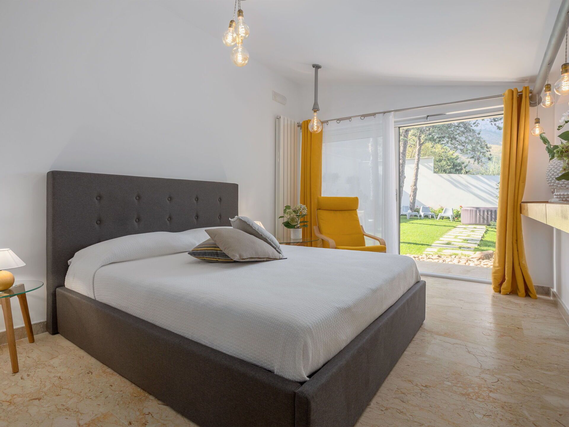 Een moderne slaapkamer met een groot bed, een tafeltje met een lamp en een stoel bij het raam.