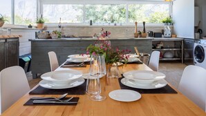 A modern kitchen with a wooden table set for dining, a sink, and a window with a view of greenery.