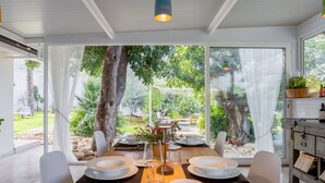 A dining area with a wooden table set for four, large windows, and a view of a garden.