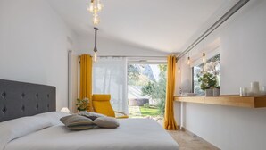 A bedroom with a bed, a chair, a window with curtains, and a shelf with decorative items.
