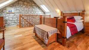 A cozy attic bedroom with a stone wall, wooden bed, and a wooden bench. - Post Office Cottage (Goodwick)