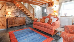 A cozy living room with a wooden staircase, a red patterned sofa, and a blue rug. - Post Office Cottage (Goodwick)