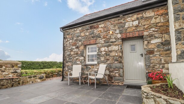 A stone building with a tiled patio, two chairs, a door, and a window. - Post Office Cottage (Goodwick)