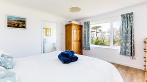 Une chambre à coucher avec un grand lit, une armoire en bois, une fenêtre avec des rideaux et un tableau accroché au mur.