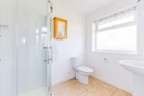 Une salle de bain avec une douche à parois de verre, des toilettes, un lavabo et une fenêtre.