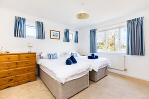 Une chambre avec deux lits, une commode en bois et une fenêtre avec des rideaux.