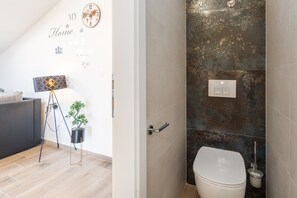 Un baño moderno con inodoro, un interruptor de luz en la pared y una lámpara de pie.