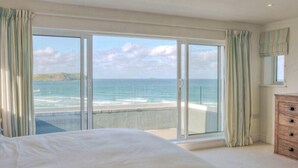 A bedroom with a large bed, a dresser, and a view of the ocean through floor-to-ceiling windows. - Treverden (Wadebridge)