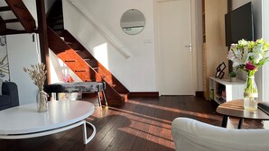 Una sala de estar moderna con una escalera, un espejo redondo, una puerta blanca y un televisor sobre un mueble de madera.