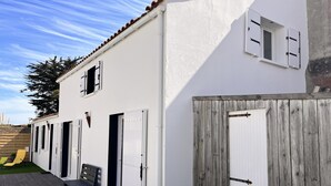 Un edificio blanco con varias puertas y ventanas, una terraza de madera con sillas y una cerca de madera.