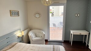 Un dormitorio con cama, una silla, una mesa y vistas a través de una puerta.
