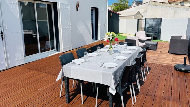 Un área de comedor al aire libre con una mesa dispuesta para seis personas, rodeada de sillas, sobre una terraza de madera.