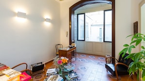 Quarto com escrivaninha de madeira, uma cadeira, planta em vaso e vista por uma porta arqueada.