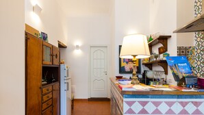 A kitchen with wooden cabinets, a tiled backsplash, a white door, and a counter with a lamp and various items. - Don Pedro Rooms Vicerè di Toledo - Camera 2 (Napoli)