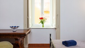 A room with a wooden table, a bed with a blue towel, and a window with a bouquet of flowers. - Don Pedro Rooms Vicerè di Toledo - Camera 4 (Napoli)