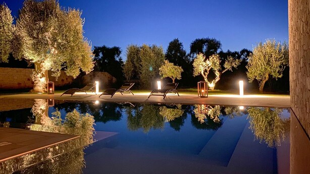 A serene outdoor pool area at dusk with reflective water, lounge chairs, and trees. - TD Villa Ricchiari Traditional Villa With Designer Pool (Fasano)