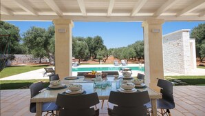 An outdoor dining area with a pool view, covered patio, and olive trees in the background. - TD Villa Ricchiari Traditional Villa With Designer Pool (Fasano)