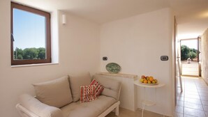 A small, well-lit room with a beige sofa, a small round table with fruit, and a view of trees through a window. - TD Villa Ricchiari Traditional Villa With Designer Pool (Fasano)