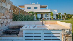 Een modern huis met een stenen muur, een barbecueplaats en een terras met tuinmeubilair.