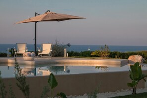 A pool area with lounge chairs and an umbrella, overlooking a body of water. - TD Villa Ponente Luxury Villa With Sea View Pool (Monopoli)