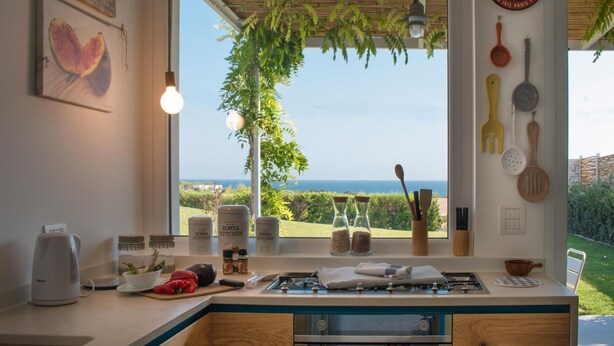 Een keuken met uitzicht op zee, een klok en keukengerei aan de muur.