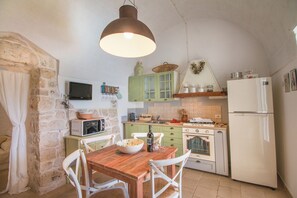 A kitchen with a wooden table, white chairs, a hanging light fixture, a stove, a microwave, and a refrigerator.