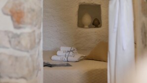 Una habitación acogedora con pared de piedra, un pequeño rincón con lámpara y adorno decorativo, y toallas ordenadamente dobladas sobre una cama.