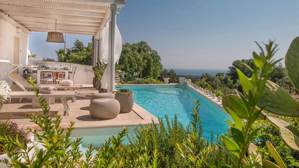 Zona de piscina con sillones reclinables, un espacio de descanso cubierto y vista al océano.