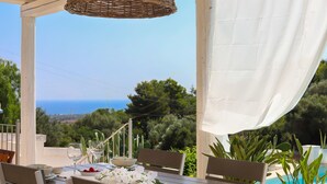 Mesa lista para comer con vista al mar, una piscina y follaje circundante.